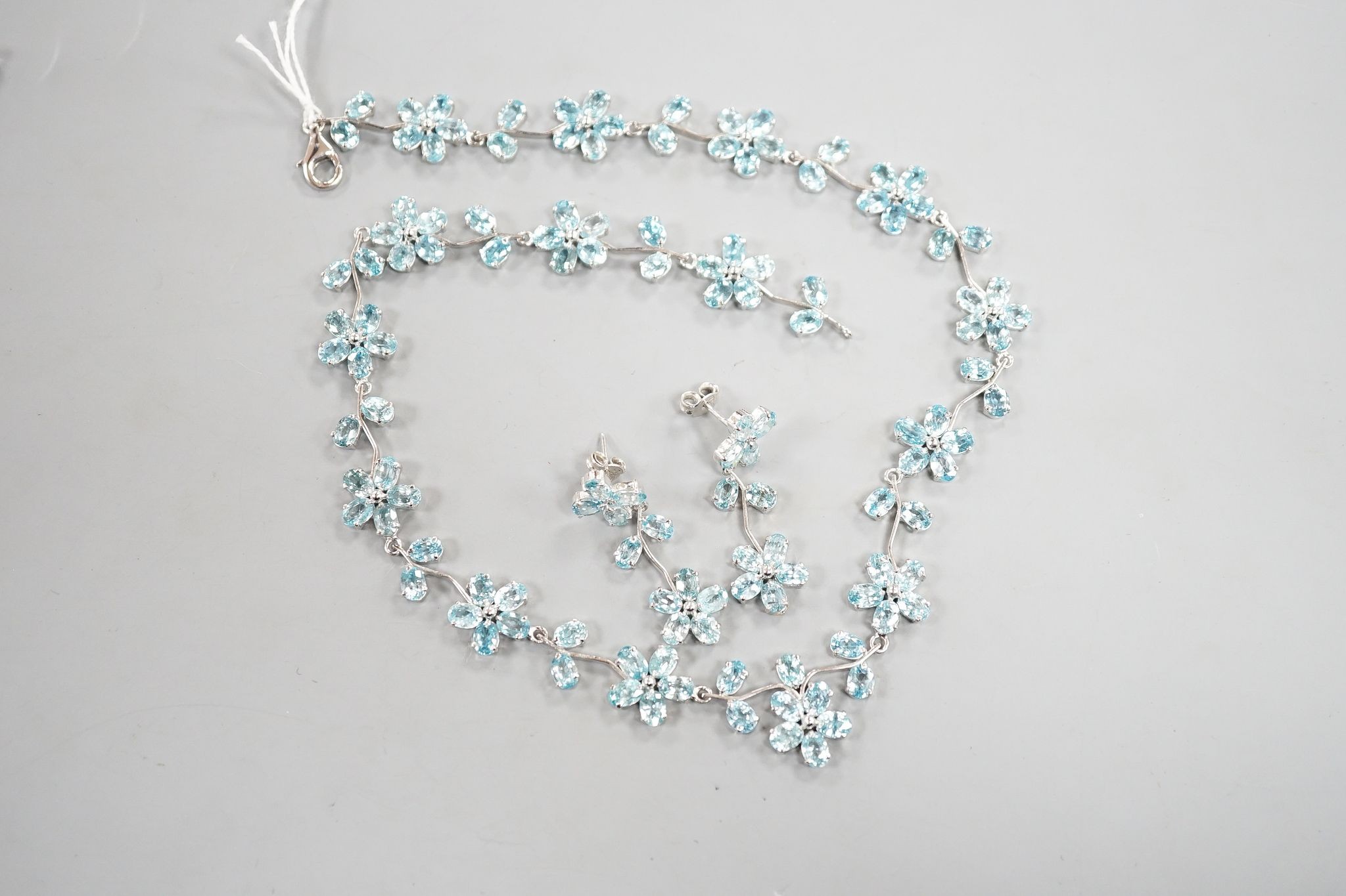 A modern 925 and blue zircon suite of jewellery, comprising a flower head cluster necklace and a pair of matching earrings.